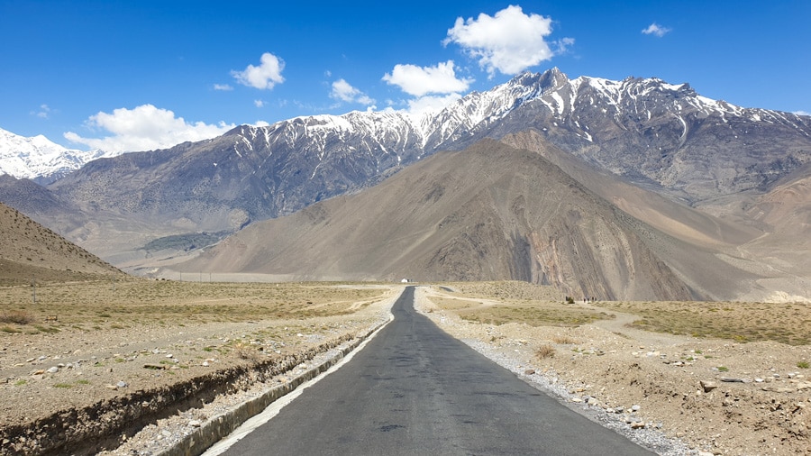 A paved road leads towards distant mountains near the village of Kagbeni