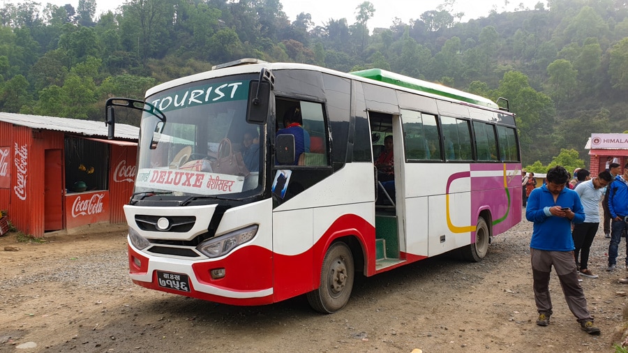 People waiting outside a parked Nepalese bus with words "tourist" and "deluxe" written on it