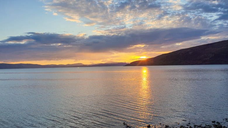 A sun setting in the distance over a still loch along the North Coast 500 in Applecross