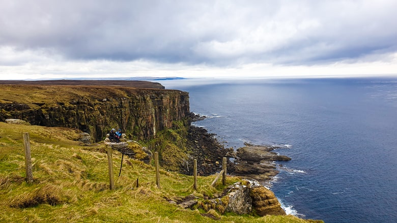 Two people resting on a rock overlooking the sea at Dunnet Head