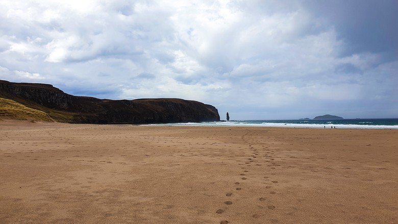 Footprints in the sand along the Sandwood Bay Beach with Am Buachaille sea stack in the distance