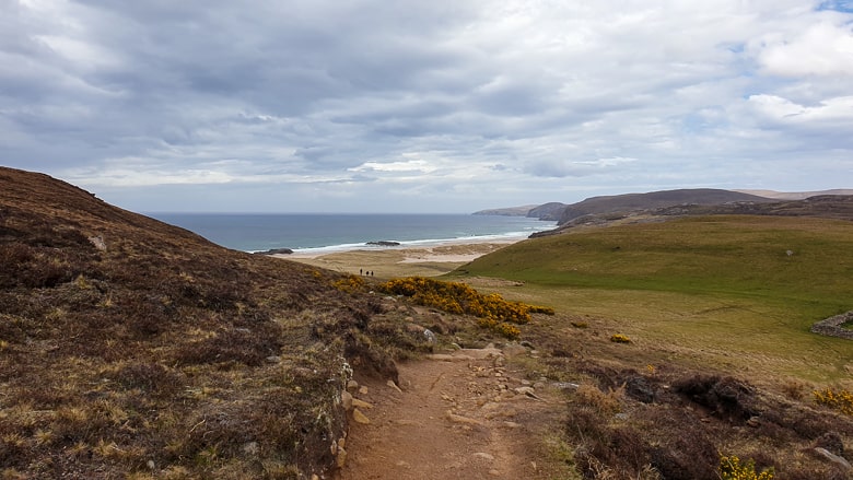 Three hikers heading to Sandwood Bay beach along a path