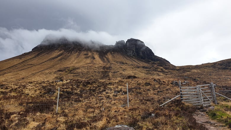 A gate along a trail heading up to cloud-covered Stac Pollaidh ridge